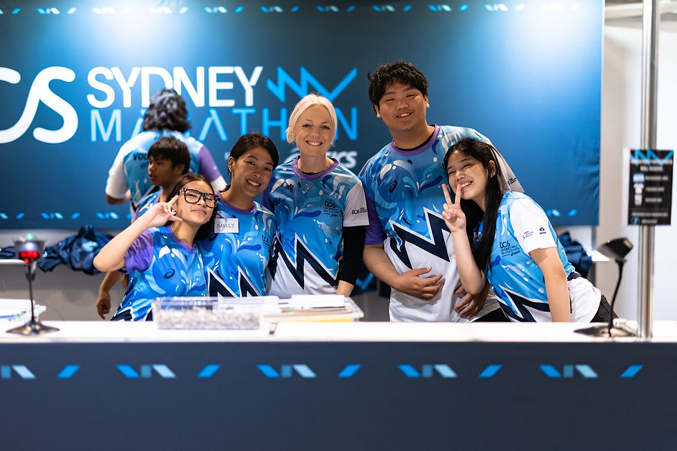Group of smiling Sydney Marathon volunteers at a booth.